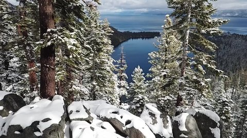 Drone flying through snowy trees towards Emerald Bay Lake Tahoe, California. partly cloudy day with fannett island in frame