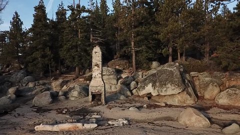 drone flys backward away from chimney beach out over the water. blue skies, forest and boulders revealed. drone rises up once out on the water with panoramic view of forest