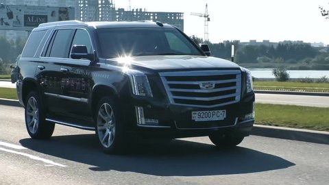 MINSK, BELARUS - AUGUST 20, 2017: Black new shiny Cadillac Escalade 6.2 V8 drives on a road on a sunny day. Escalade is a full-size luxury SUV, most most identifiable model of Cadillac.