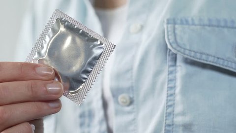 Girl hands holding sealed condom, putting it into pocket of shirt, contraception