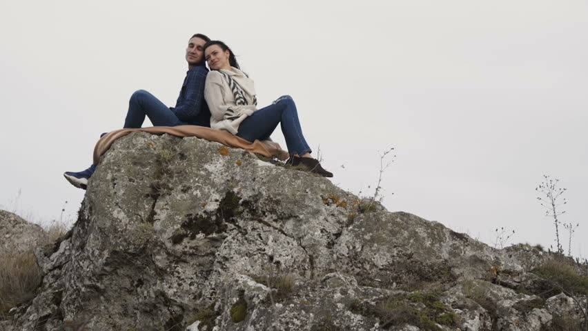 Lovely couple resting in embraces on the top stones of a rock in windy day. 4K