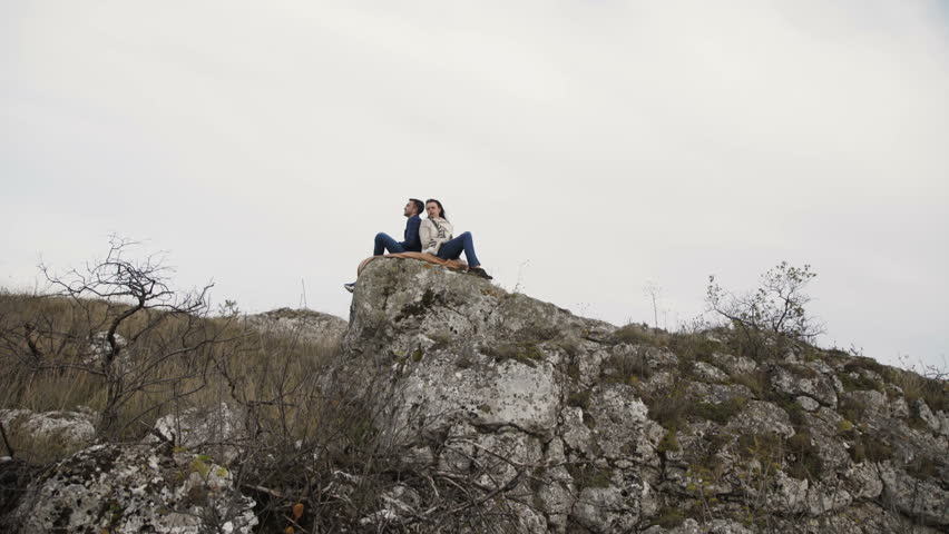 Lovely couple resting in embraces on the top stones of a rock in windy day. 4K