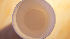 close up HD video of coffee and milk pouring into paper cup, hand takes cup away from right side.