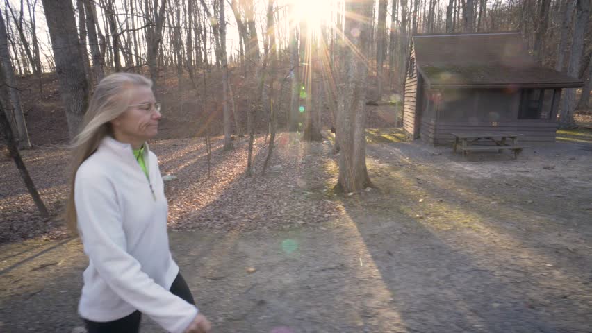 Mature blonde woman hiking past a state park cabin in a forest in West Virginia.
