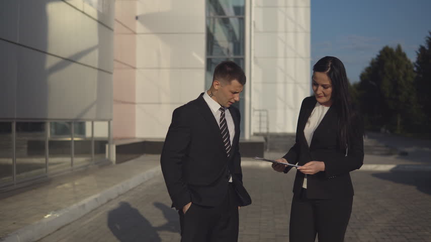 Business meeting. Young beautiful businesswoman talks and shows documents to young male employee outdoors against backdrop of business center Royalty-Free Stock Footage #33704158