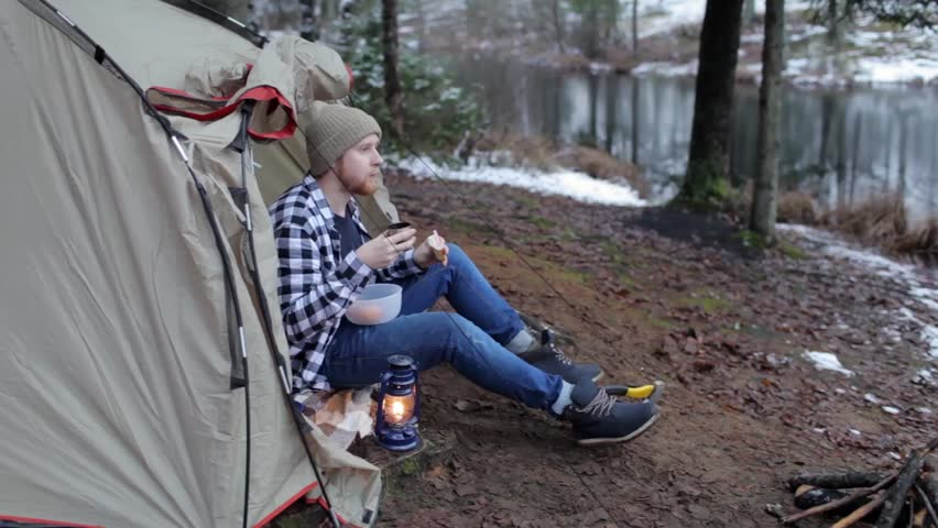 tourist is drinking tea with sandwiches sitting in a tent on the lake shore