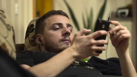 Medium shot of man listening music on cellphone on bed