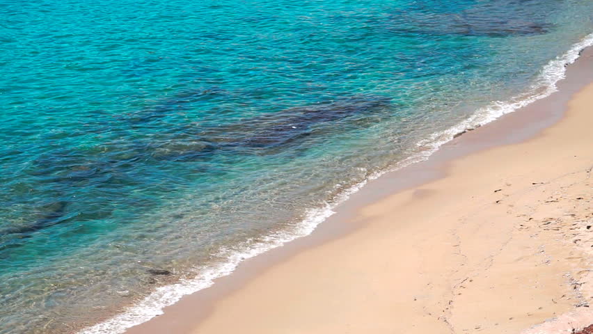 Turquoise crystal clear Aegean sea water waves breaking gently on a sandy beach coast line. Mykonos island, Greece.