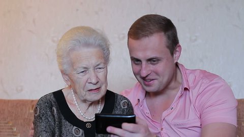 Grandmother with grandson having fun at home. They are together looking at the smartphone screen and laughing