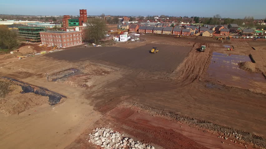 An aerial shot of a muddy constuction site. A village surrounds the site.