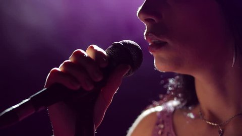 Close-up of the face of the singer with microphone on a black smoky background. The singer sings a song on stage in the dark, smoke, purple light, concert.