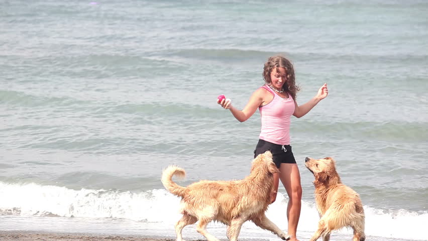 Beautiful happy woman playing with two dogs at beach