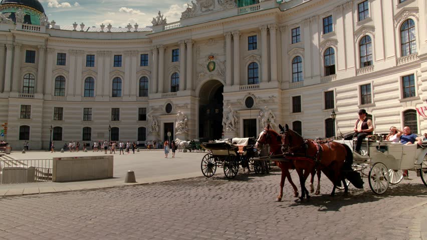 A viennese Coach, so called „Fiaker“ passes by at the Michaelerplatz at this wide angle shot of the „Wiener Hofburg“, Sky is replaced.

Variation without: "Vienna Hofburg  with Fiaker - tilt up". Royalty-Free Stock Footage #33740239