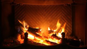 Round logs burn in fireplace. Ancient brass fire iron corrects burning coals. Man hand puts  next log into fire. HD video