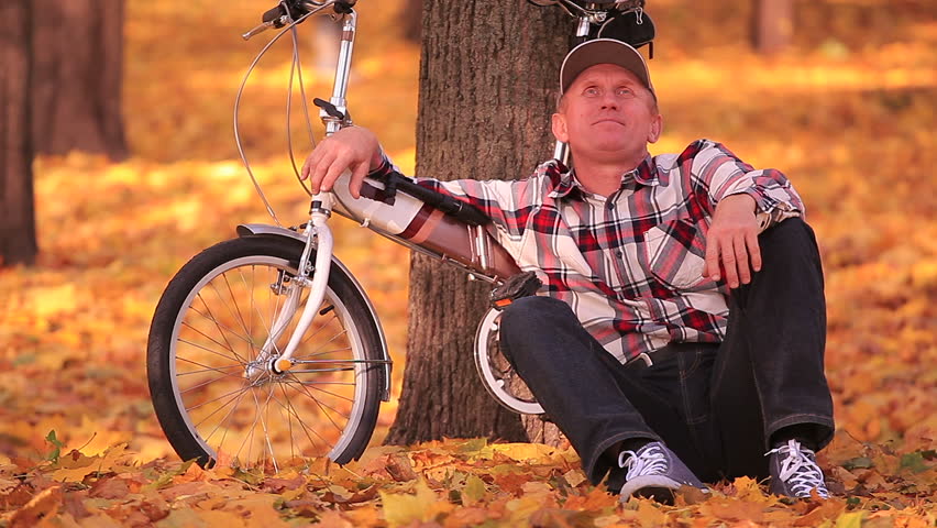 Adult man sit near  small bicycle  in  autumn park with yellow trees