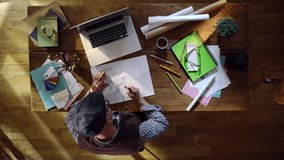 Top view. Architect working in his office. He draws a kitchen on a piece of paper and consults his laptop computer. Video