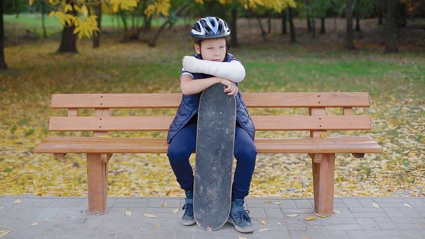 Caucasian child with broken arm sitting on the bench with skate. Failure concept.
