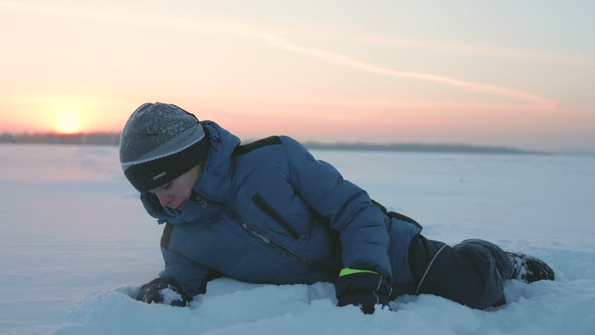 the child is lying on snow and looking at the sunset. winter Park