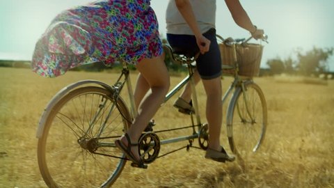 Young man and woman riding a bicycle tandem on rural field and haystacks. Couple woman and man cycling bike tandem on summer field on background nature landscape