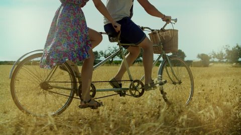 Couple man and woman riding a bicycle tandem on background summer field and haystacks. Young woman and man cycling bike tandem on rural field in summer day