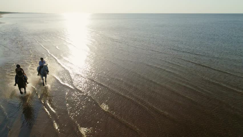 Two women riding horses on a beach