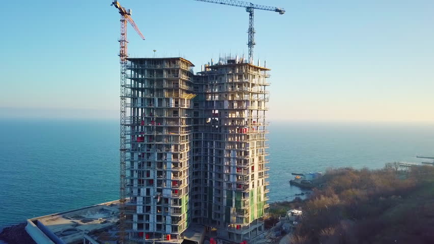 Aerial city view. Construction of a high-rise skyscraper on the ocean by two cranes. Even slow travel. Royalty-Free Stock Footage #33764044