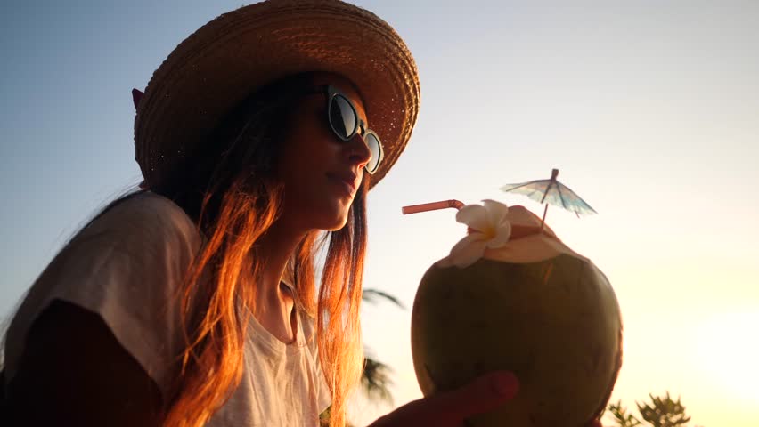 Attractive Young Tourist Hipster Girl Drinking Fresh Thai Coconut Water Cocktail at the Beach Against Beautiful Sunset. 4K, Slowmotion. Phuket, Thailand. Royalty-Free Stock Footage #33769894