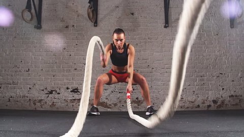 Athletic Female Actively in a Gym Exercises with Battle Ropes During Her Cross Fitness Workout. Slow motion