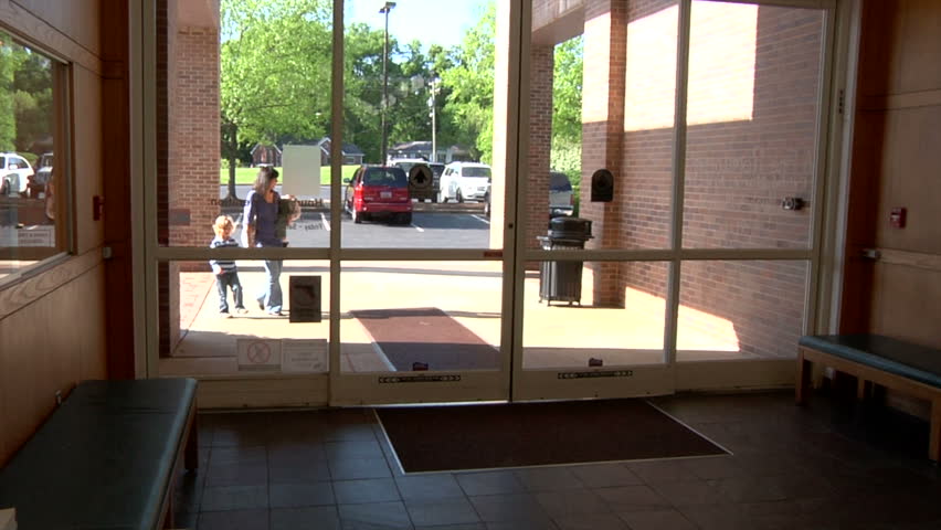 Kids enter library with mom to get books to read. Young family walking into library for education material for homeschool.