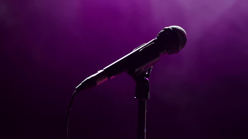Microphone in hand singer on stage. Close-up. Silhouette of singer on stage with microphone in hand. Dark background, smoke, spotlights. Royalty-Free Stock Footage #33778132