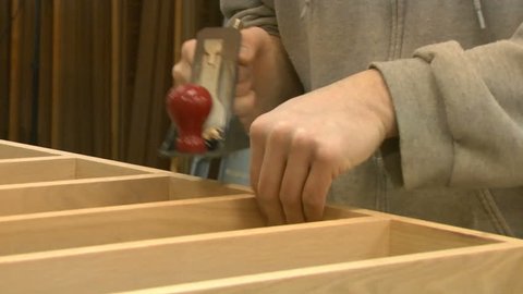 A woodworker craftsman uses a manual hand plane to make fine changes to a wood project, in this case a shelf unit.