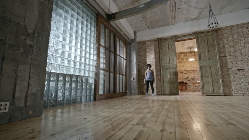 Zoom in with PAN of determined black woman in fitness outfit standing against brick wall in empty loft and looking into camera