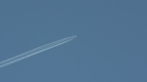 Jet plane flies in the blue sky, leaving a small vapor trail. Zoom