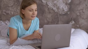 young caucasian woman has online video call at home. attractive blonde girl lying on bed looking on screen laptop talking with friend