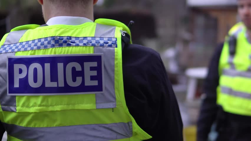 Detail Of Police Uniform Writing With Two Male Police Officers Talking And Surveying Outdoor Area. High Vis Yellow Jacket. British Law Enforcement. Royalty-Free Stock Footage #33805636