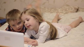 Children on the bed with a laptop. little boy and girl watching shows online. Children look at the cartoon.