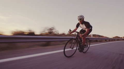 Young Fit Man Cycling On Road Bike Outside At Sunset Racing Downhill