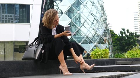 Businesswoman Rests With Coffee Outdoors Feeling Pain After Wearing High Heels. 4K. 