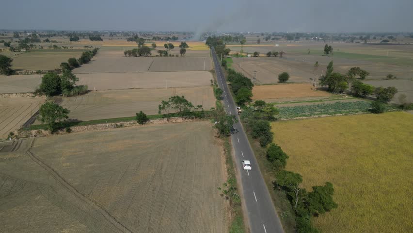Beautiful drone shot following the car on the road in the farms.
