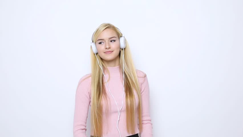 Blonde woman listen music on headphone and dance flirting and bite her lips on white background