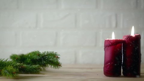 New Year's footage. Two lit candles and a branch of a Christmas tree on a wooden background. It's snowing.