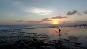 Evening video of Bali island with silhouette children running on seashore washed by warm waves.Aerial marine scenery of tropical beach with beautiful sunset 