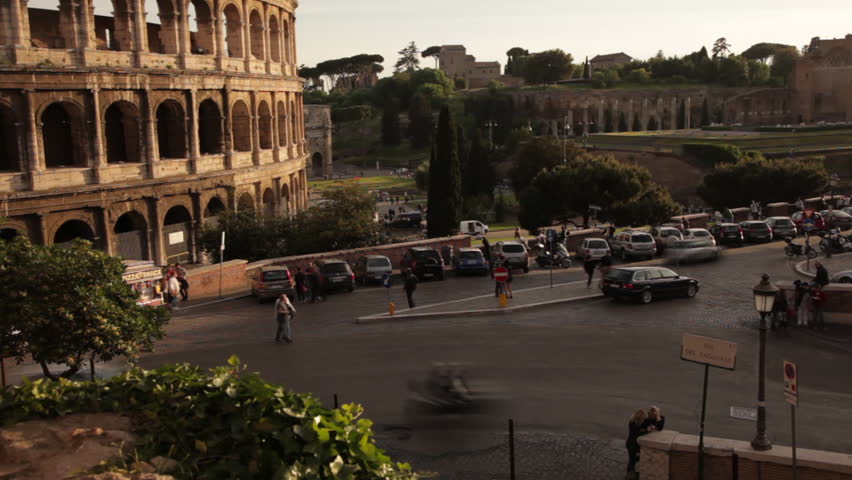 Cars driving by the Colosseum seen from nearby park.