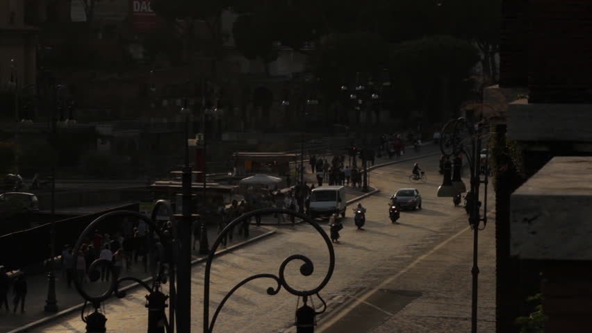 Cars, mopeds, bicycles, and pedestrians on street near the Colosseum.