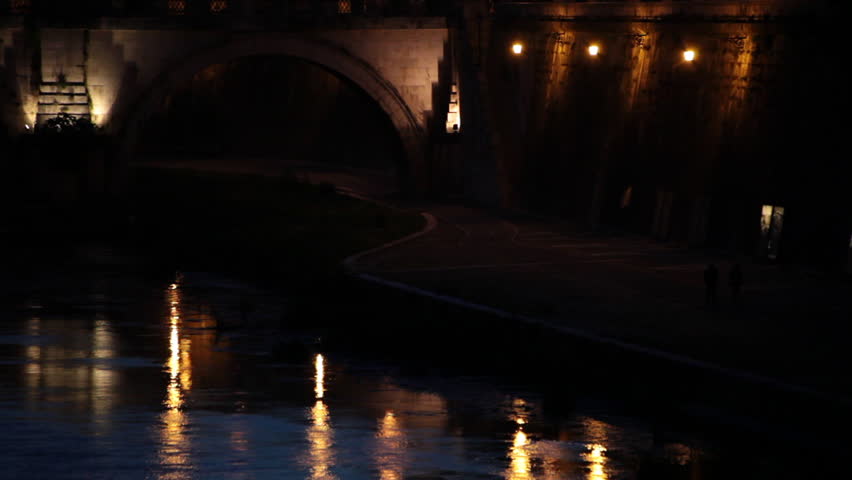 Reflections of a dim lit building and archway on a canal in Rome Italy