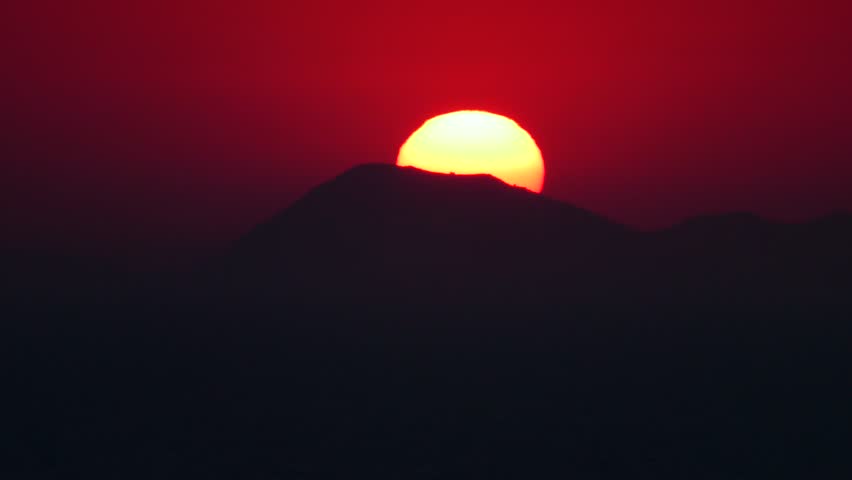 The sun sets over a distant mountain, time lapse.