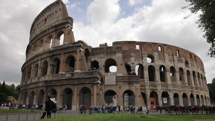 View of the Colosseum with tourists walking around and horse carriages seen off