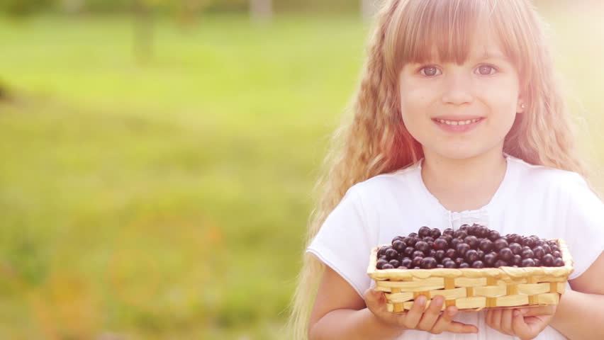 Sunny girl. Closeup portrait of child holding a basket of black currant. Lens