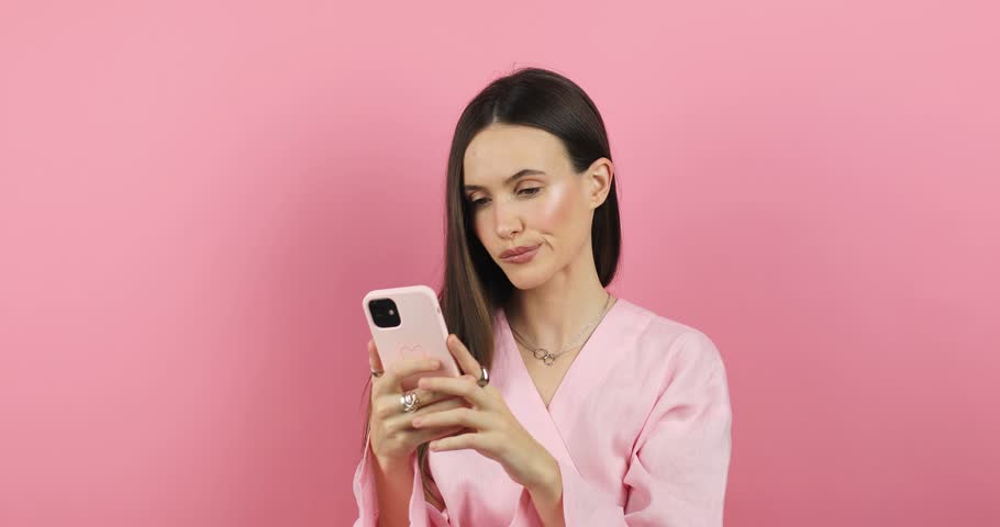 Close up brunette woman touch face, pensive think problem solution looking at mobile phone. Thoughtful girl thinking idea browsing smartphone chat isolated pink background, woman not sure. Royalty-Free Stock Footage #3383457697