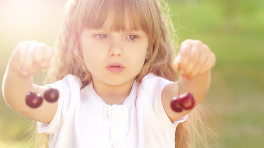 Sunny kid playing with a sweet cherry fruit